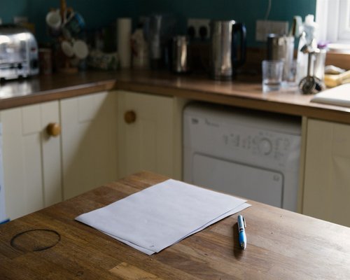 A pair of human hands neatly writing down a daily schedule in a paper notebook on a sunny kitchen table